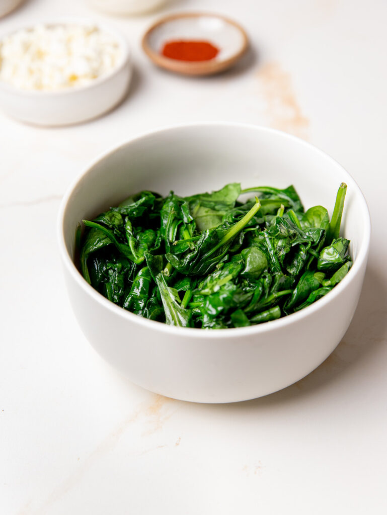 Spinach in a white bowl for spinach stuffed chicken recipe.