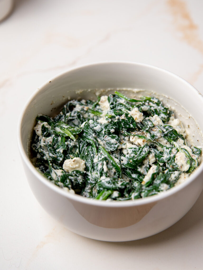 Spinach and feta in a white bowl for spinach stuffed chicken recipe.