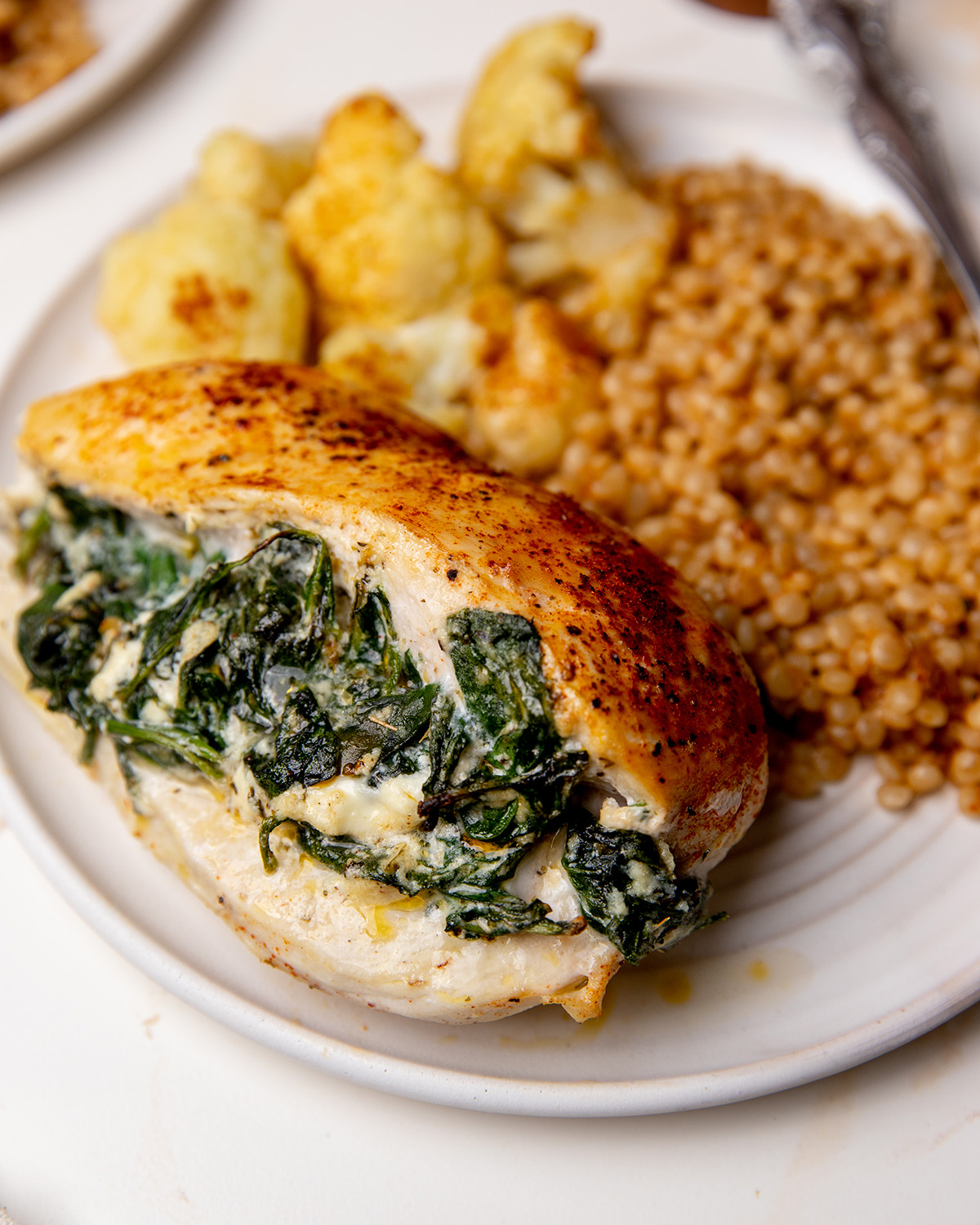 A plate of spinach stuffed chicken with cous cous and cauliflower.