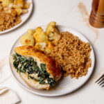 Spinach stuffed chicken on a white place with cous cous and cauliflower.