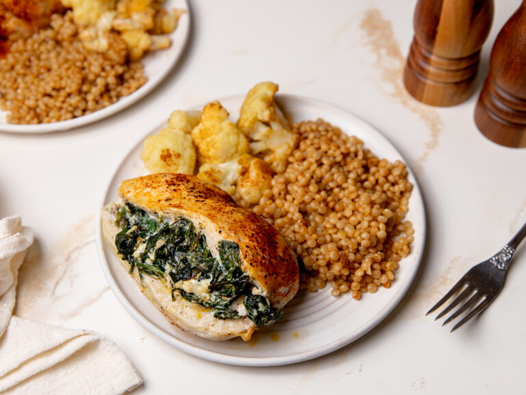 Spinach stuffed chicken on a white place with cous cous and cauliflower.