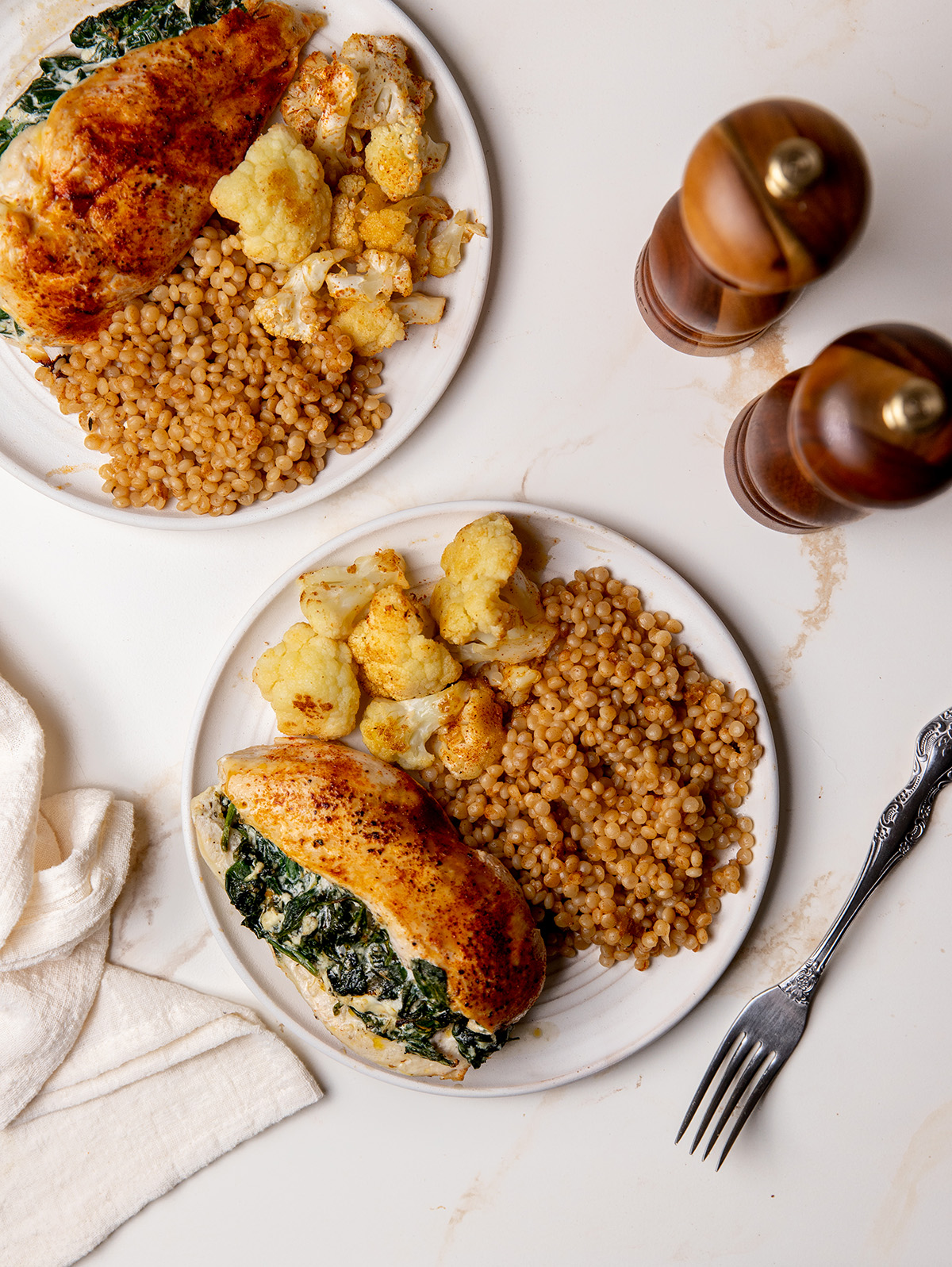 Two servings of spinach stuffed chicken on white plates over a white marble surface.