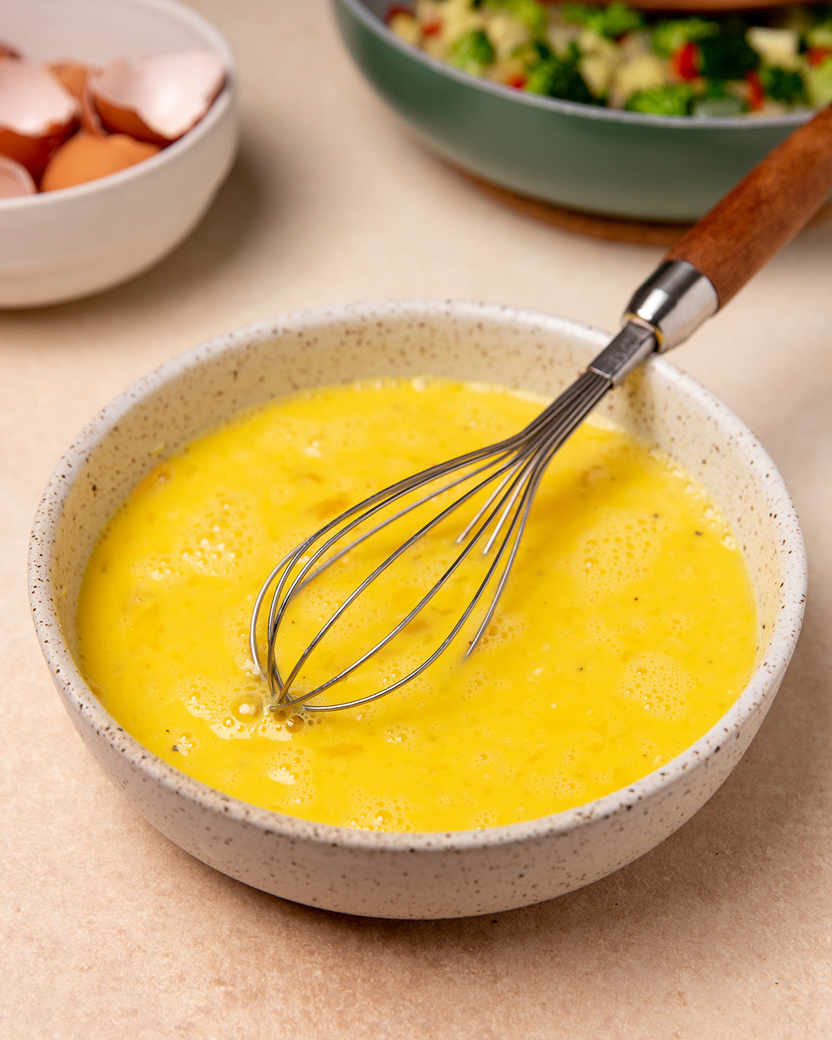 Whisked eggs in a white bowl with whisk.