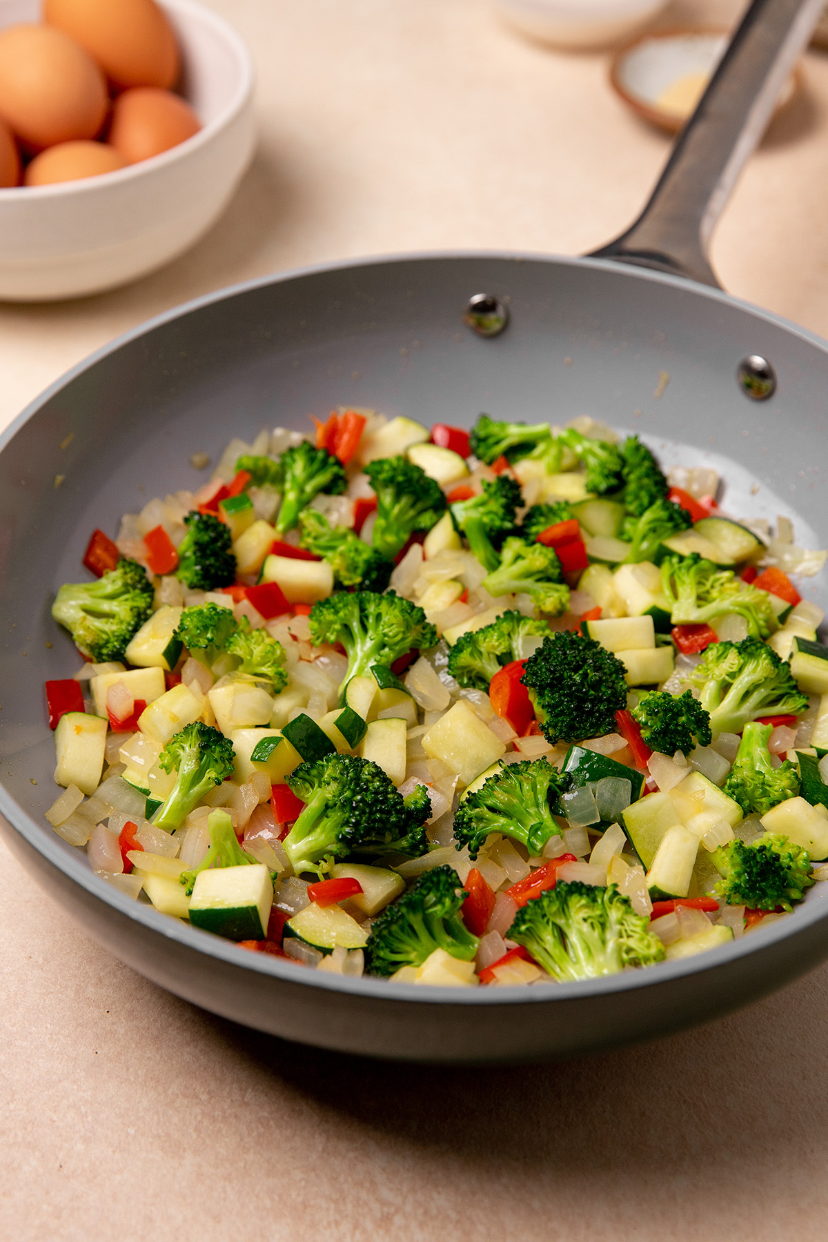 Broccoli, onion, and bell peppers getting sauteed in a pan.