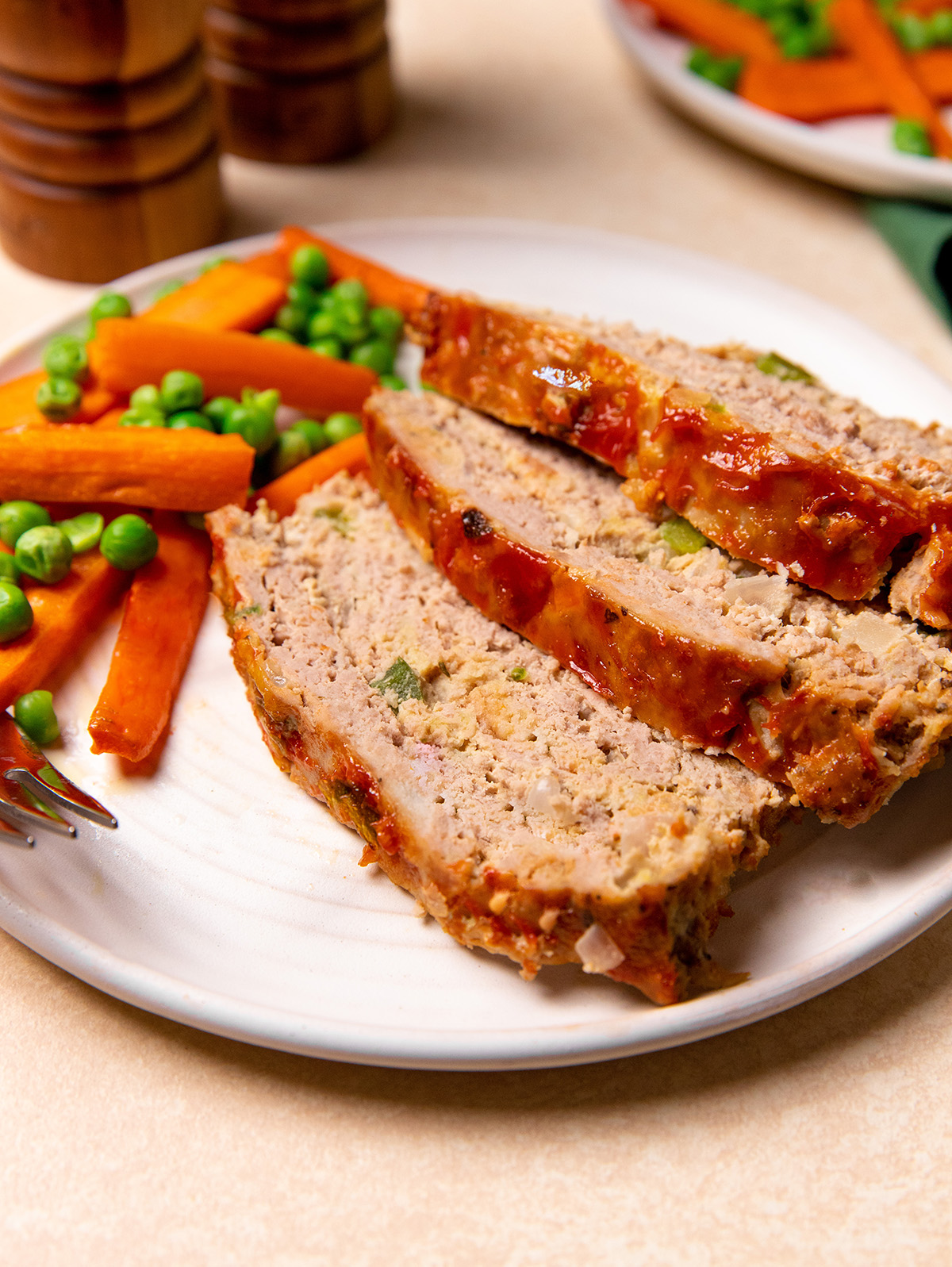 Low-sodium turkey meatloaf on a white plate with a side of carrots and peas.