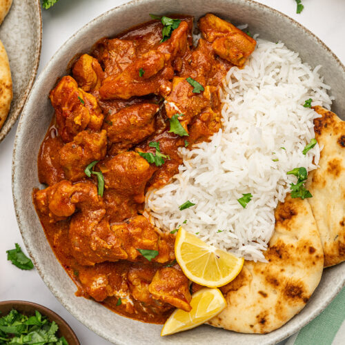 Low sodium butter chicken served on a plate with naan bread, a lemon wedge, and a side of basmati rice.