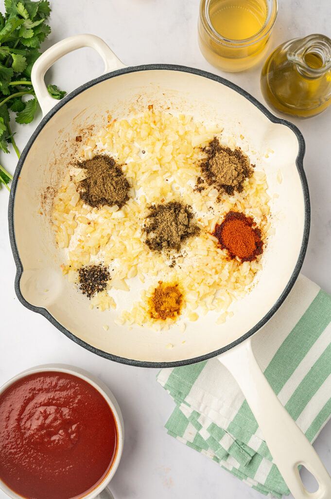 Spices toasting in a skillet with onions, garlic, and ginger for low sodium butter chicken recipe.