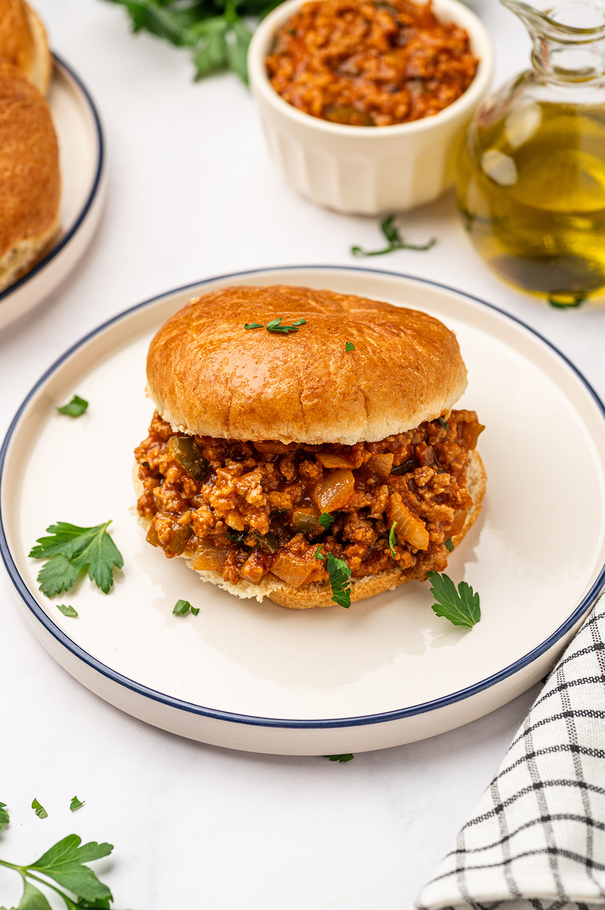 A low sodium sloppy joes sandwich on a bun, garnished with fresh parsley and served on a minimalist white plate.