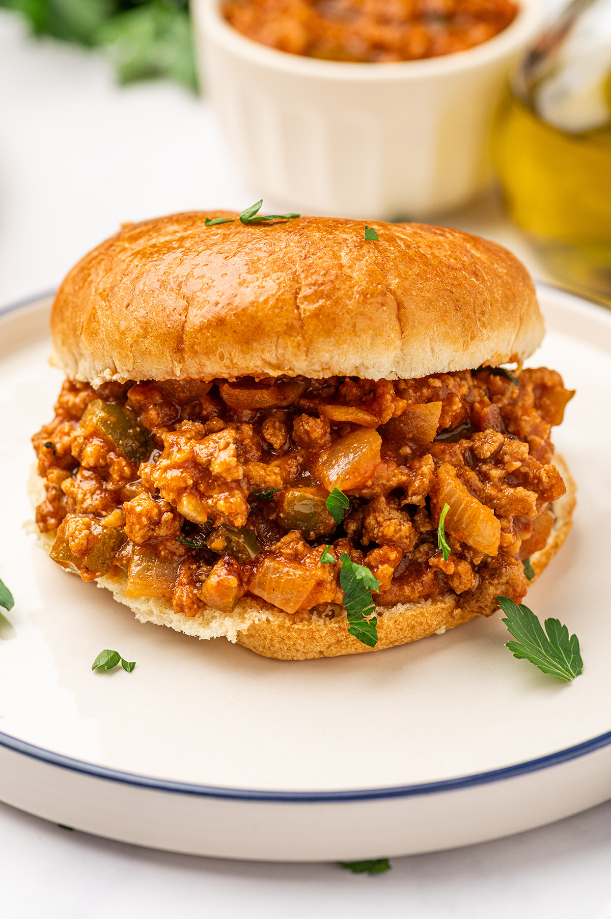 A low sodium sloppy joes sandwich on a toasted bun, garnished with fresh parsley and served on a white plate.