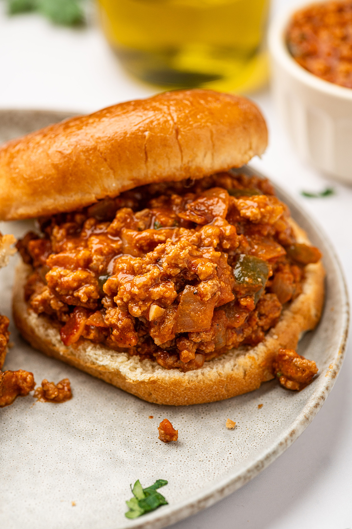 A messy, delicious low sodium sloppy joes sandwich on a bun, with parsley sprinkled on top and served on a clean white plate.