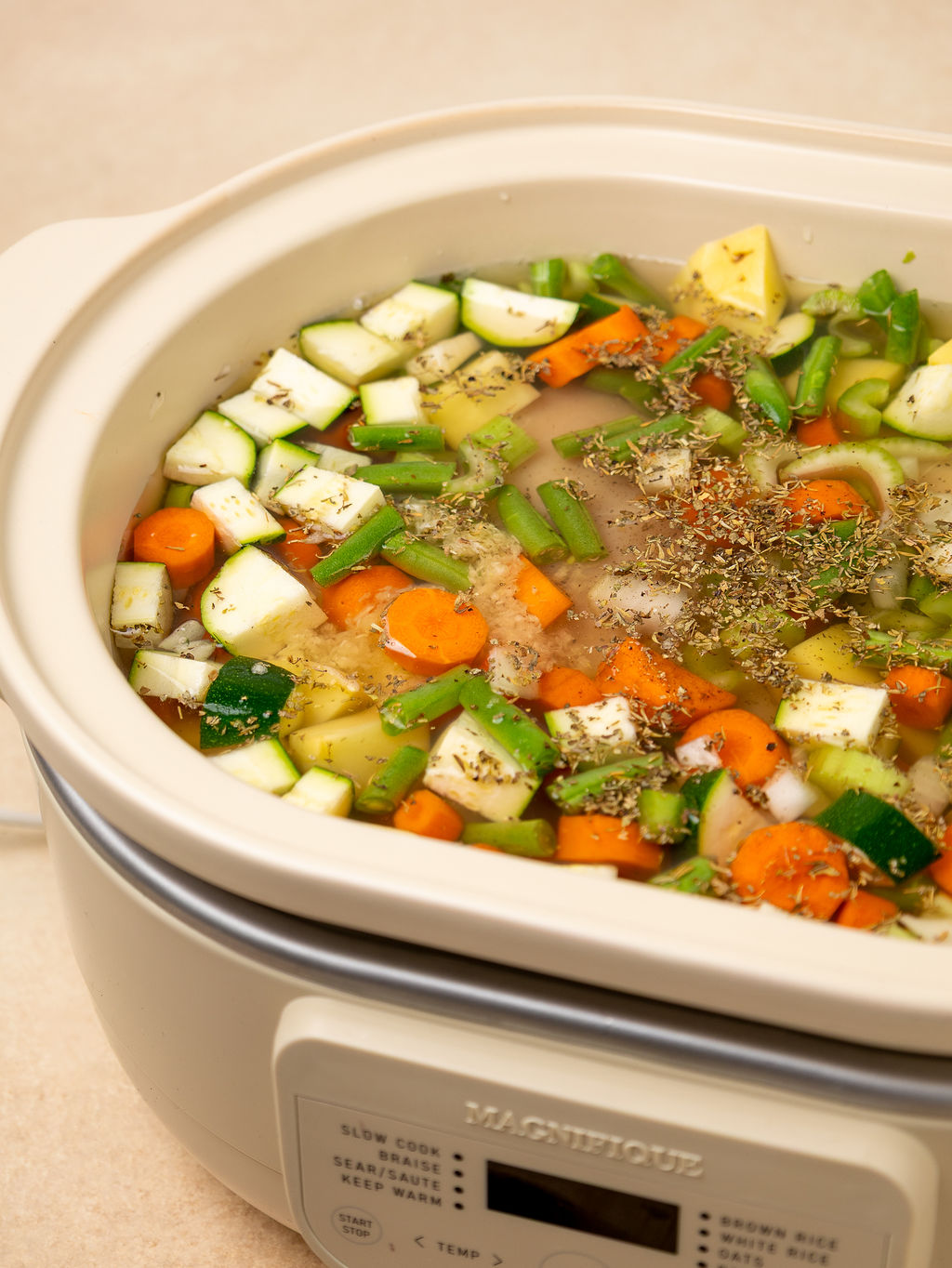 Veggies, broth, and seasonings in a slow cooker ready to cook.