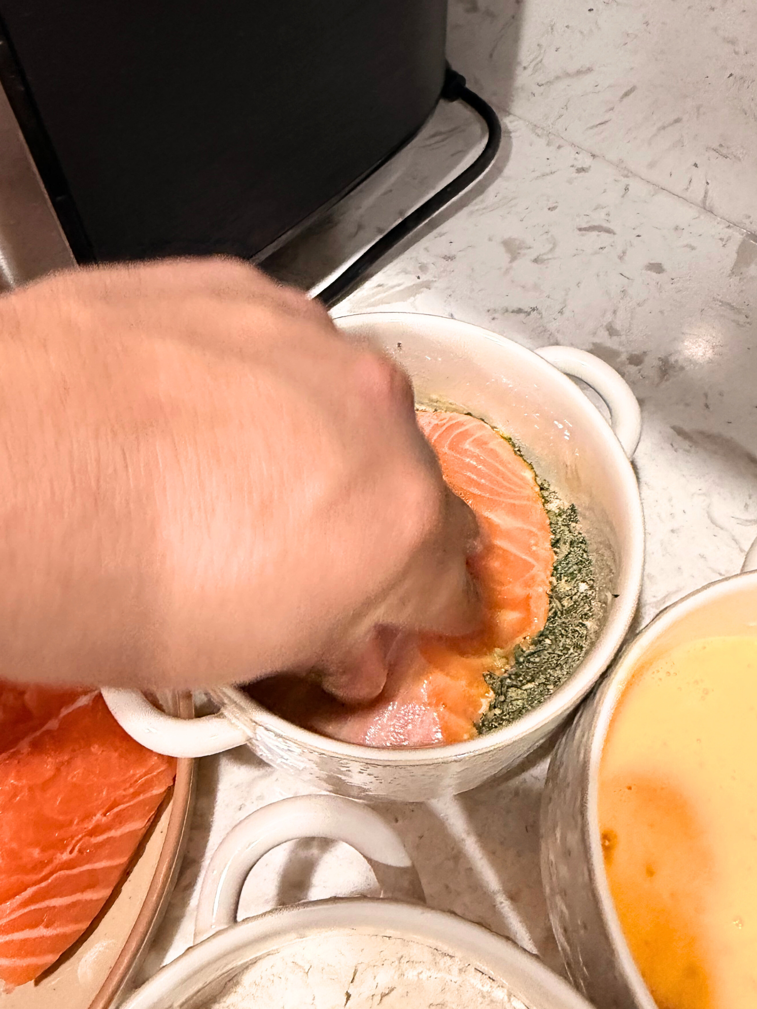 Dipping salmon into a breadcrumb mixture.